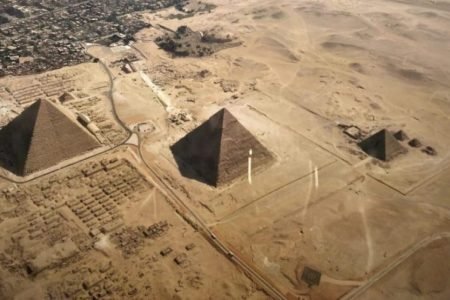Una veduta aerea ad alta quota delle tre principali Piramidi di Giza (Khufu, Khafre e Menkaure) e della Grande Sfinge, circondate dal deserto sabbioso e adiacenti all'espansione urbana del Cairo, in Egitto.